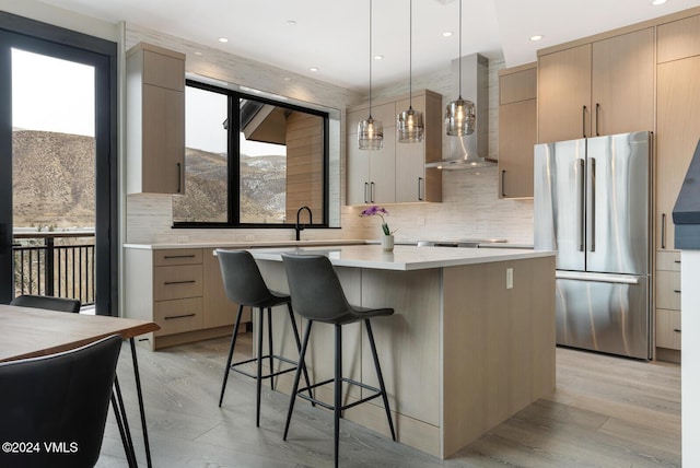 kitchen with light brown cabinets, a center island, wall chimney range hood, and stainless steel refrigerator