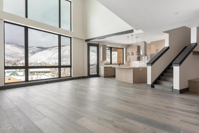 unfurnished living room featuring a towering ceiling, a mountain view, sink, and light wood-type flooring