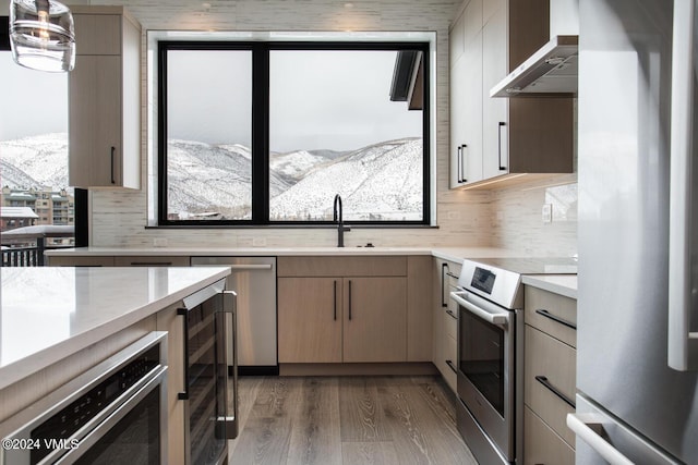 kitchen featuring appliances with stainless steel finishes, tasteful backsplash, wine cooler, a mountain view, and wall chimney range hood