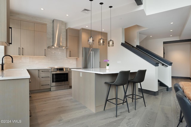 kitchen featuring sink, stove, light brown cabinetry, high end refrigerator, and wall chimney exhaust hood