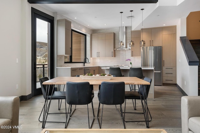 kitchen with stainless steel refrigerator, a center island, light brown cabinetry, decorative light fixtures, and wall chimney exhaust hood