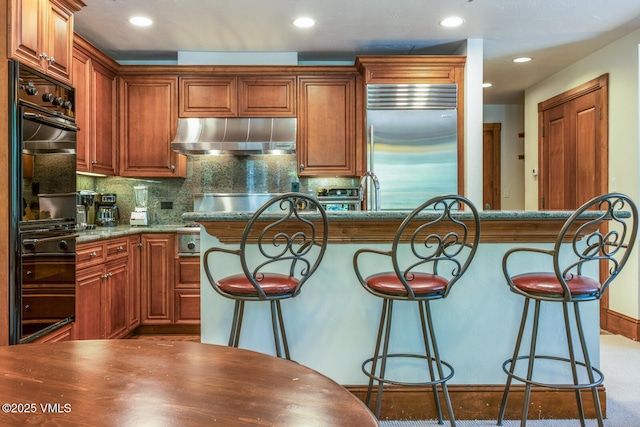 62 Highlands Ln Unit R103, R102, Beaver Creek, CO 81620 - kitchen with stainless steel built in refrigerator, exhaust hood, a breakfast bar, decorative backsplash, and recessed lighting