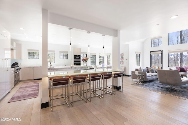 kitchen featuring multiple ovens, pendant lighting, white cabinets, and light hardwood / wood-style floors