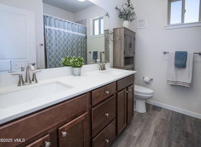 bathroom featuring double vanity, wood finished floors, a sink, and toilet