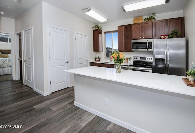 kitchen featuring dark brown cabinetry, dark wood finished floors, stainless steel appliances, and light countertops