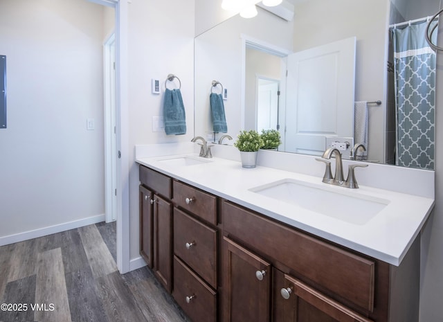 bathroom with double vanity, baseboards, a sink, and wood finished floors