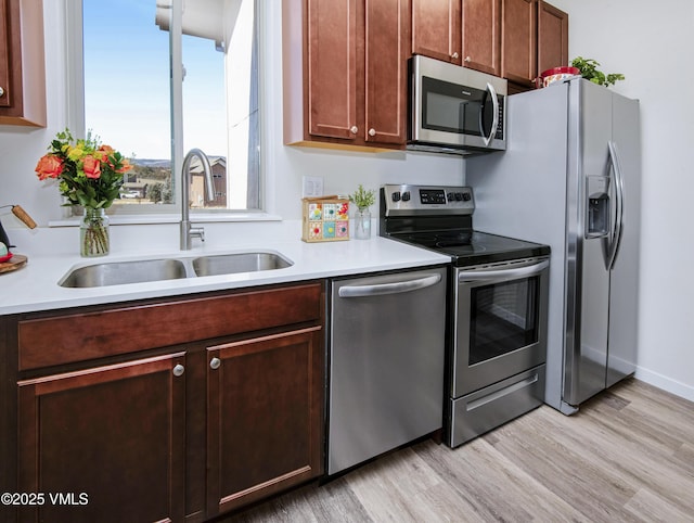 kitchen with appliances with stainless steel finishes, light wood-style floors, light countertops, and a sink