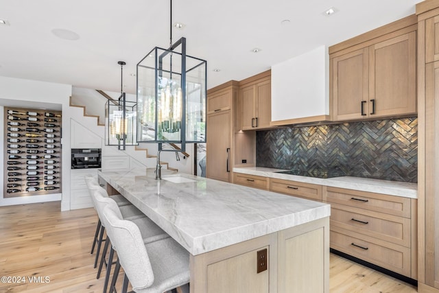 kitchen featuring sink, a kitchen island with sink, black electric cooktop, decorative light fixtures, and light wood-type flooring