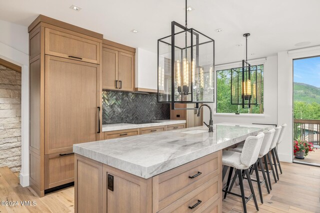 kitchen featuring pendant lighting, sink, an island with sink, and tasteful backsplash