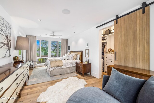 bedroom with ceiling fan, a walk in closet, a barn door, and light wood-type flooring