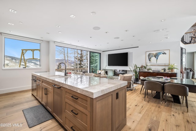 kitchen featuring sink, light wood-type flooring, a mountain view, an island with sink, and light stone countertops