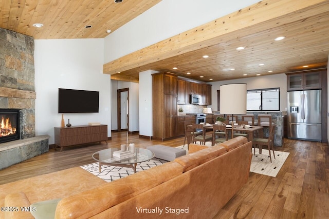 living area with recessed lighting, wood ceiling, a stone fireplace, and wood finished floors