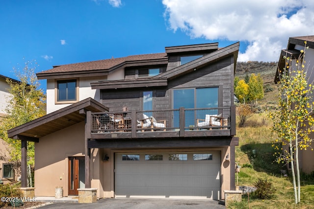 rear view of house featuring a garage, a balcony, aphalt driveway, and stucco siding