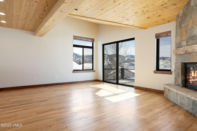 unfurnished living room with light wood finished floors, wood ceiling, vaulted ceiling with beams, a fireplace, and a mountain view