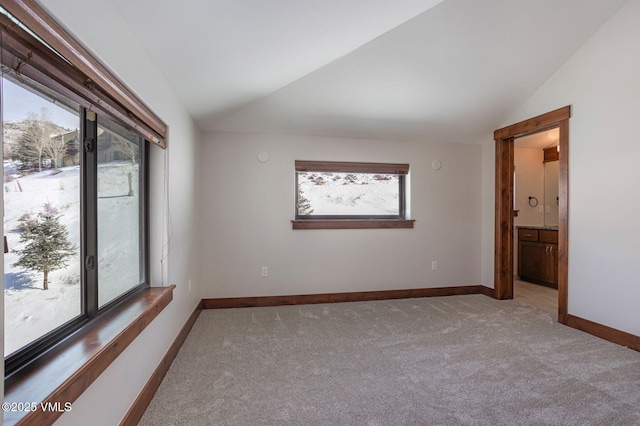 spare room featuring lofted ceiling, baseboards, light colored carpet, and a healthy amount of sunlight