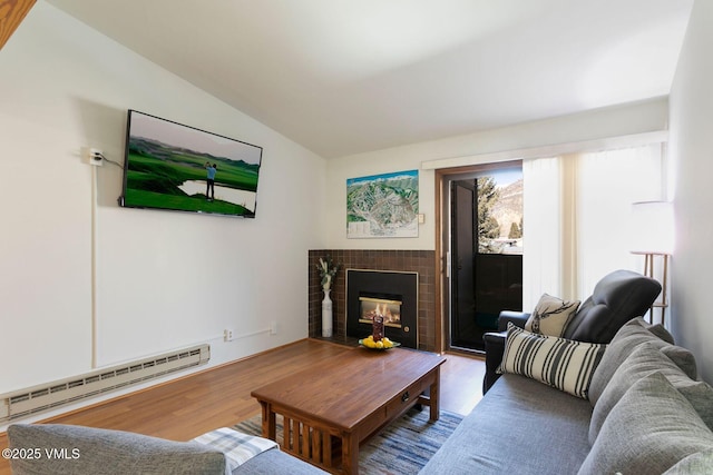 living room with vaulted ceiling, a tile fireplace, a baseboard radiator, and wood finished floors