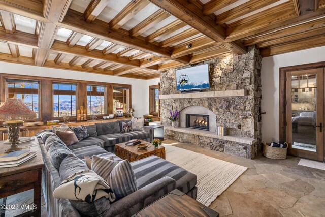 living room with coffered ceiling, a stone fireplace, and beamed ceiling