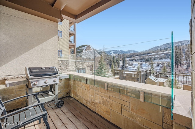 snow covered deck featuring a mountain view and area for grilling