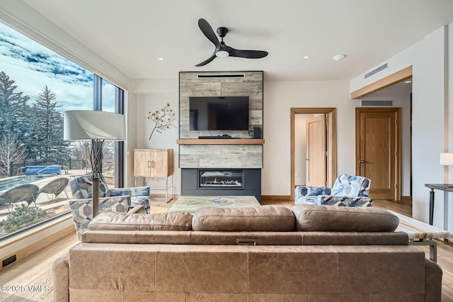 living area with a fireplace, wood finished floors, visible vents, and a ceiling fan