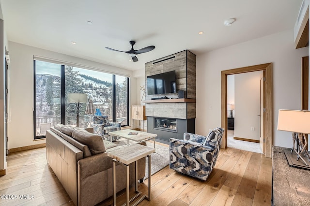 living area with light wood-type flooring, a tile fireplace, a ceiling fan, and baseboards