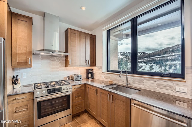 kitchen featuring a sink, appliances with stainless steel finishes, wall chimney range hood, and brown cabinets