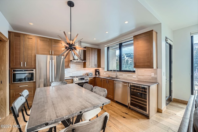 kitchen with tasteful backsplash, wine cooler, stainless steel appliances, wall chimney range hood, and a sink