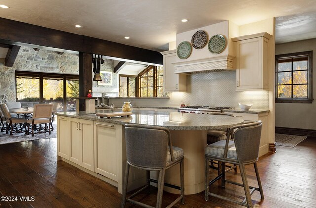 kitchen featuring beamed ceiling, dark hardwood / wood-style floors, a center island with sink, and decorative backsplash