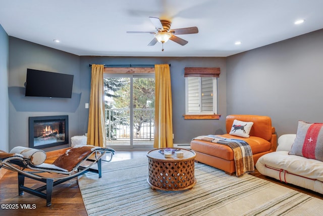 living room with ceiling fan, hardwood / wood-style floors, and a baseboard heating unit