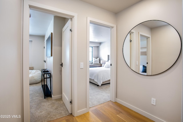 hallway featuring light wood finished floors, baseboards, and light colored carpet