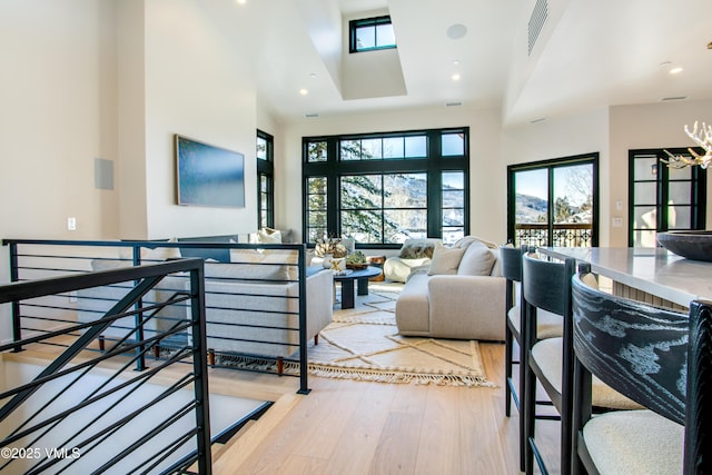 living room with light wood-style floors, recessed lighting, visible vents, and a towering ceiling