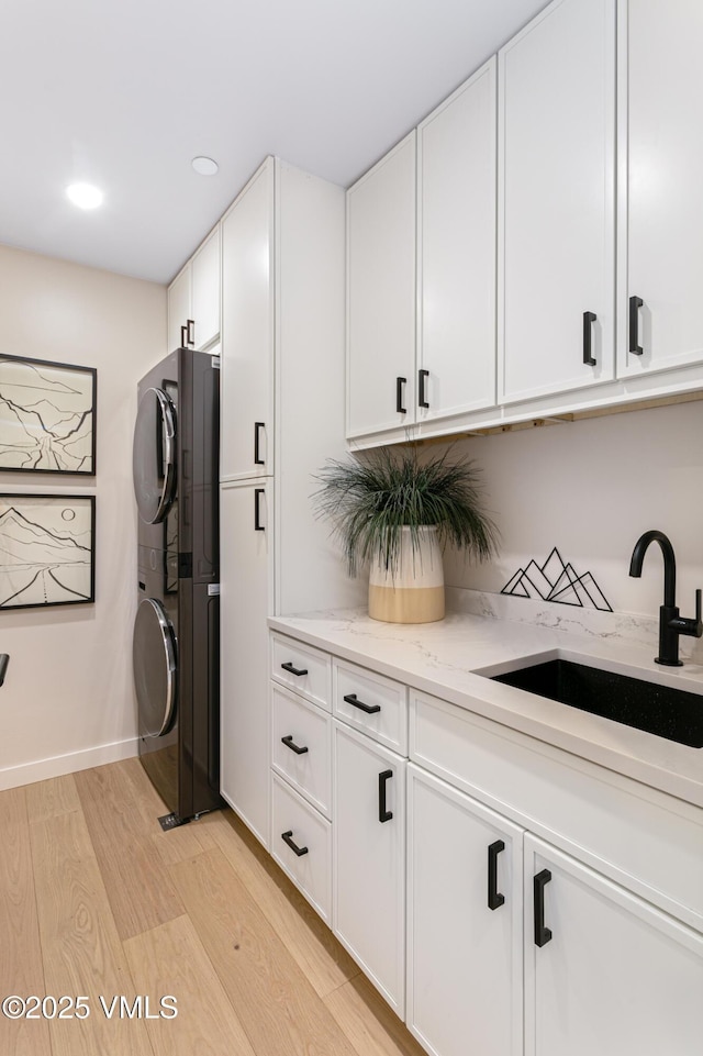 kitchen featuring light stone counters, light wood finished floors, stacked washer / dryer, white cabinetry, and a sink