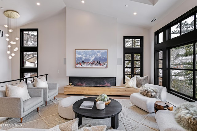 living area featuring recessed lighting, visible vents, a glass covered fireplace, wood finished floors, and high vaulted ceiling