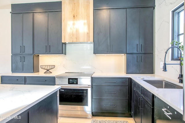 kitchen featuring light stone counters, stainless steel electric range oven, backsplash, and a sink