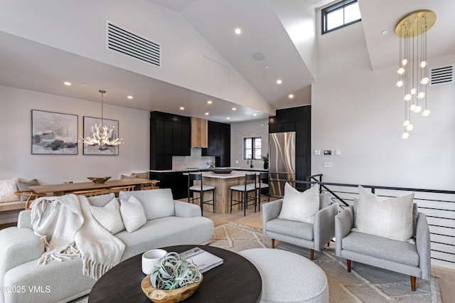 living area with high vaulted ceiling, visible vents, light wood-style floors, and an inviting chandelier