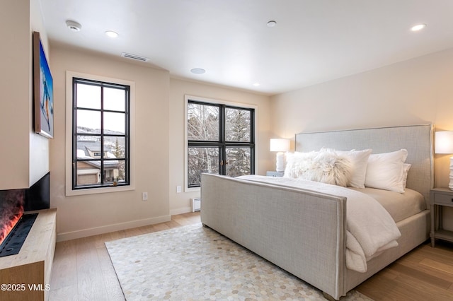 bedroom with baseboards, visible vents, light wood-type flooring, a baseboard heating unit, and recessed lighting