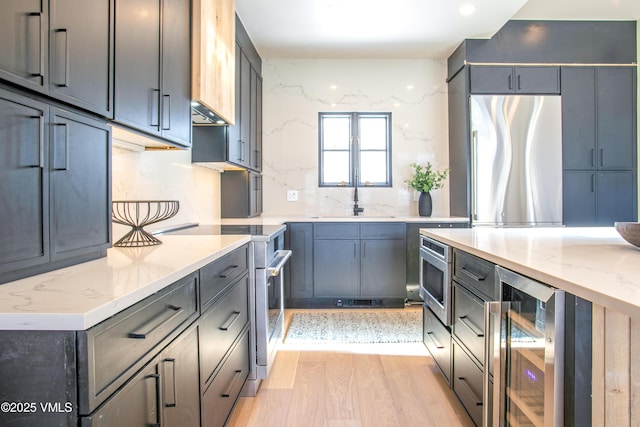 kitchen featuring stainless steel appliances, wine cooler, a sink, and light stone counters