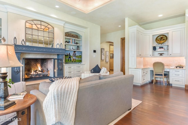 living room featuring dark hardwood / wood-style floors, built in desk, a high end fireplace, and built in shelves