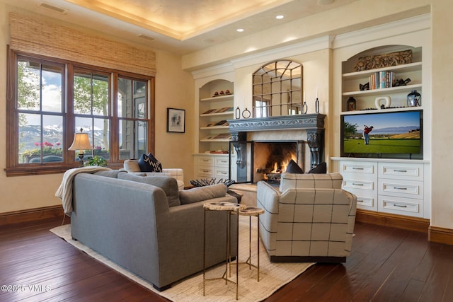 living room featuring a raised ceiling, dark hardwood / wood-style flooring, built in features, and a high end fireplace