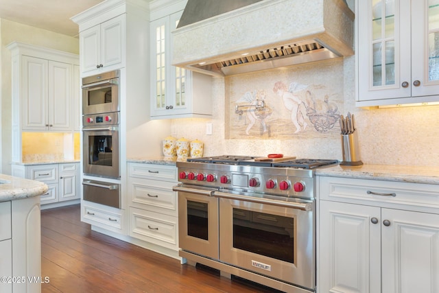 kitchen featuring appliances with stainless steel finishes, white cabinets, custom exhaust hood, light stone countertops, and dark wood-type flooring