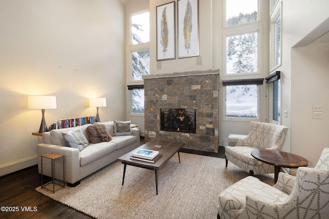 living room with dark hardwood / wood-style flooring, a stone fireplace, and a high ceiling