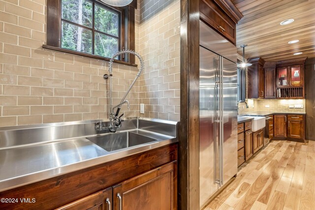 kitchen with tasteful backsplash, sink, stainless steel counters, and light hardwood / wood-style flooring