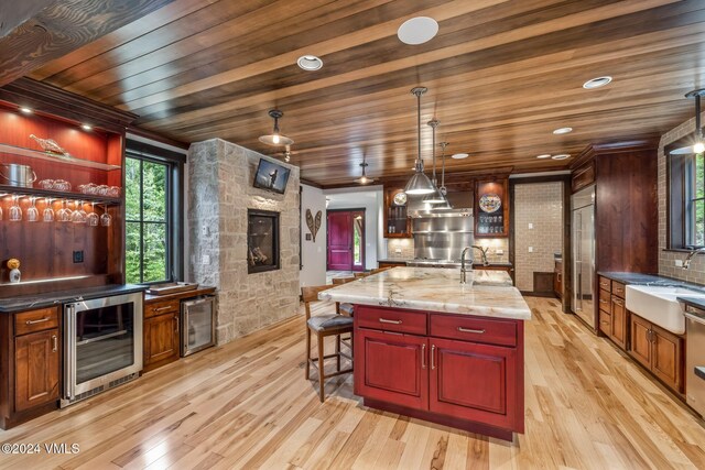 kitchen featuring an island with sink, sink, wine cooler, and decorative light fixtures