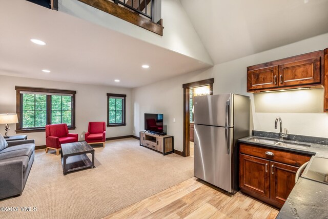 kitchen with high vaulted ceiling, sink, light colored carpet, and stainless steel refrigerator