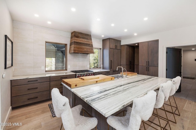 2036 Vermont Rd, Vail, CO 81657 - kitchen with modern cabinets, custom exhaust hood, a breakfast bar area, a large island with sink, and light wood-style floors