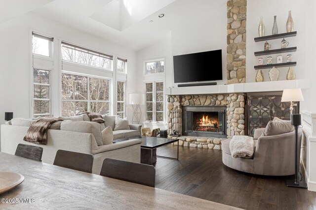 living area with a skylight, a fireplace, high vaulted ceiling, and wood finished floors