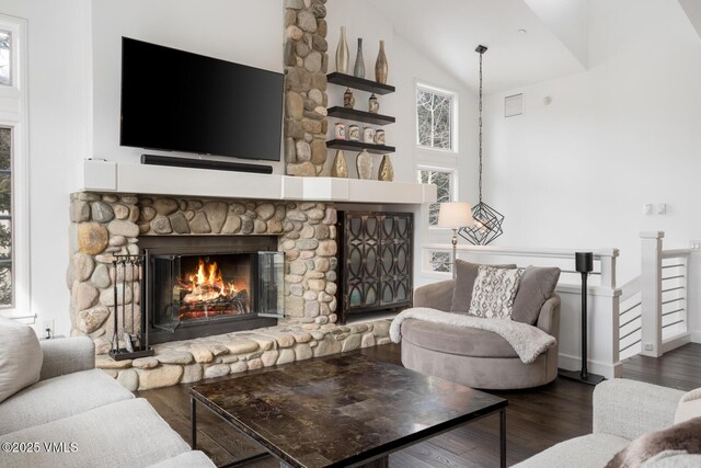 living room with a stone fireplace, wood finished floors, baseboards, and high vaulted ceiling