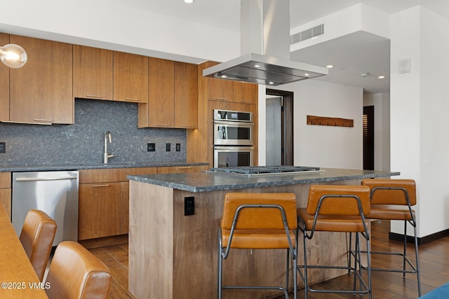 kitchen featuring dark wood-style flooring, decorative backsplash, appliances with stainless steel finishes, island range hood, and a sink