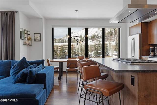 kitchen with wood finished floors, freestanding refrigerator, dark countertops, wall chimney exhaust hood, and open floor plan