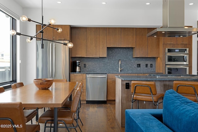 kitchen featuring island exhaust hood, stainless steel appliances, a wealth of natural light, and brown cabinetry