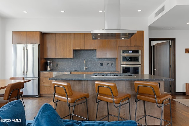 kitchen featuring visible vents, dark wood-type flooring, island range hood, stainless steel appliances, and a sink